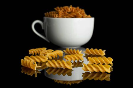 Lot of whole dry brown wholegrain fusilli in white ceramic cup isolated on black glassの写真素材