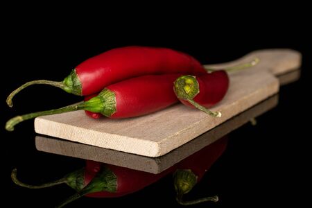 Group of three whole hot red chili cayenne on wooden cutting board isolated on black glassの写真素材