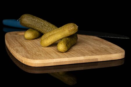 Group of four whole sour green pickle crossed on bamboo cutting board with steel knife isolated on...