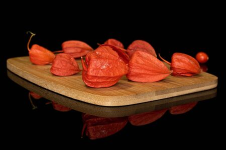 Group of nine whole fresh orange physalis on bamboo cutting board isolated on black glassの写真素材