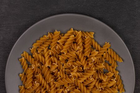 Lot of whole dry brown wholegrain fusilli on gray ceramic plate flatlay on grey stoneの写真素材