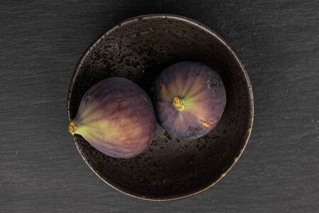 Group of two whole sweet purple fig on glazed bowl flatlay on grey stoneの写真素材