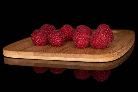 Lot of whole fresh red raspberry on bamboo cutting board isolated on black glass