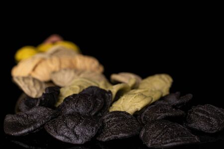 Lot of whole colored colorful pasta orecchiette isolated on black glass
