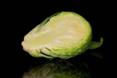 One half of fresh green brussels sprout isolated on black glass