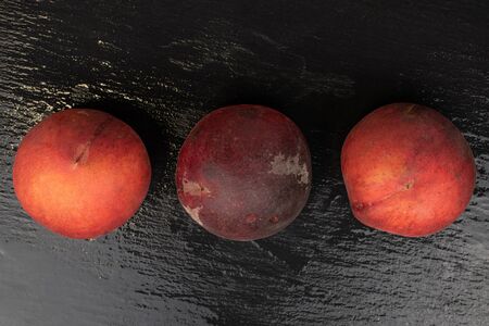 Group of three whole sweet red peach in row flatlay on grey stoneの写真素材