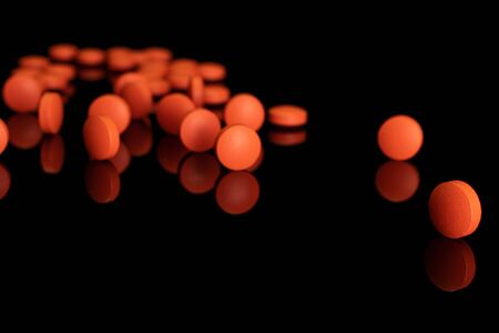 Lot of whole disordered orange tablet pharmacy isolated on black glassの写真素材