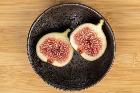 Group of two halves of sweet purple fig on glazed bowl flatlay on light woodの写真素材