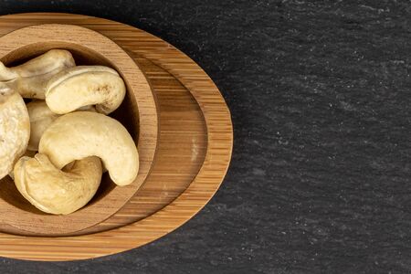 Lot of whole brown nut cashew on round bamboo coaster in bamboo bowl flatlay on grey stoneの写真素材
