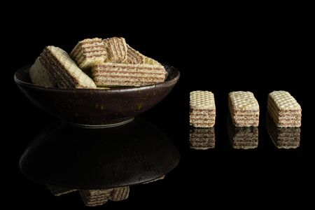 Lot of whole crispy beige hazelnut wafer cookie in dark ceramic bowl isolated on black glassの写真素材