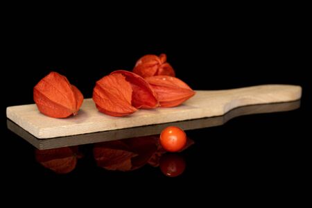 Group of five whole fresh orange physalis on wooden cutting board isolated on black glassの写真素材