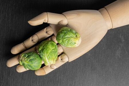 Group of three whole fresh green brussels sprout with wooden hand flatlay on grey stoneの写真素材