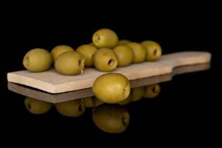 Group of eleven whole marinated green olive on wooden cutting board isolated on black glass