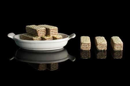 Group of eight whole crispy beige hazelnut wafer cookie in white oval ceramic bowl isolated on black glassの写真素材