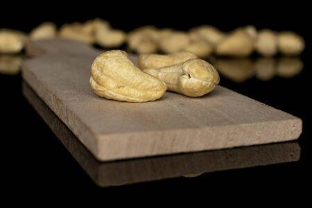 Lot of whole brown nut cashew two in focus on wooden cutting board isolated on black glass
