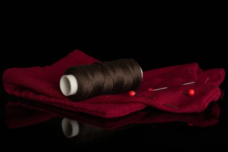 One whole haberdashery item dark brown thread spool with needles on fabric isolated on black glass