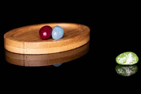 Group of three whole jelly bean candy on round bamboo coaster isolated on black glassの写真素材