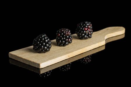 Group of three whole fresh black blackberry on small wooden cutting board isolated on black glass