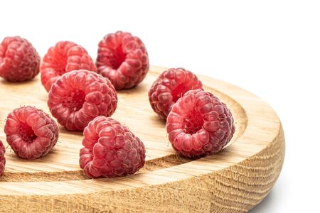 Lot of whole fresh crimson raspberry on bamboo plate isolated on white background