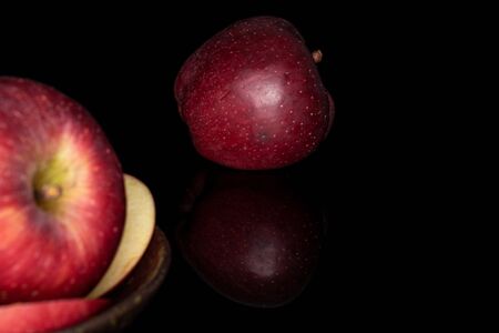 Group of two whole two slices of fresh apple red delicious on glazed bowl isolated on black glassの写真素材