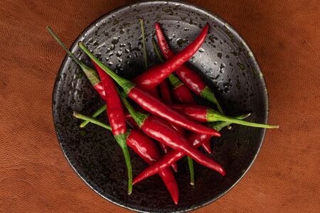 Lot of whole hot red chili on glazed bowl flatlay on cognac leatherの写真素材