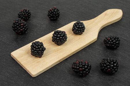 Lot of whole fresh black blackberry on small wooden cutting board on grey stoneの写真素材