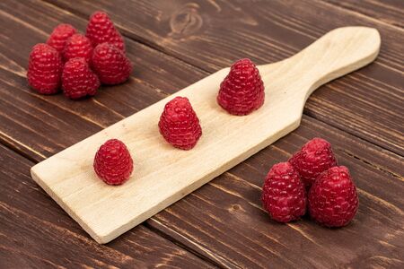Lot of whole fresh red raspberry on small wooden cutting board on brown woodの写真素材