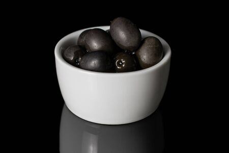 Lot of whole canned black olive in white sauce bowl isolated on black glassの写真素材