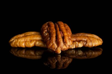 Group of three whole dry brown pecan nut isolated on black glass