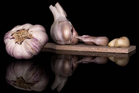Group of two whole four pieces of aromatic white garlic on wooden cutting board isolated on black glassの写真素材