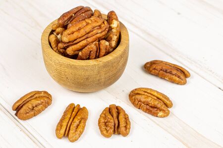 Lot of whole dry brown pecan nut in tiny wooden bowl on white wood