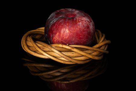 One whole fresh red plum in wiker nest isolated on black glassの写真素材