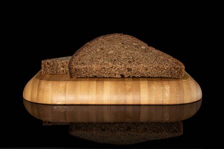 Group of two slices of fresh baked dark bread on wooden square plate isolated on black glass