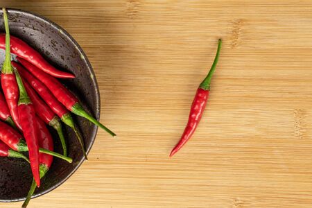 Lot of whole hot red chili on glazed bowl one separated flatlay on light woodの写真素材