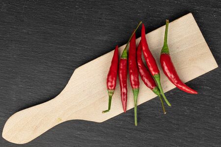 Lot of whole hot red chili on wooden cutting board flatlay on grey stone