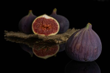 Group of three whole one half of fresh purple fig on natural sackcloth isolated on black glass