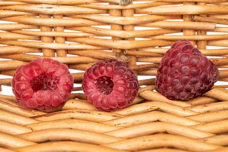 Group of three whole fresh crimson raspberry with braided rattan behind