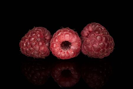 Group of four whole fresh crimson raspberry isolated on black glass