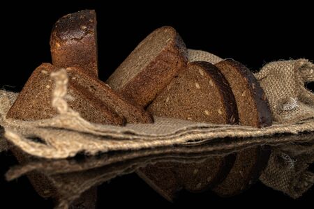 Group of two halves four slices of fresh baked dark bread on jute cloth isolated on black glass