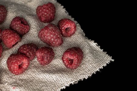 Lot of whole fresh crimson raspberry on jute cloth isolated on black glassの写真素材