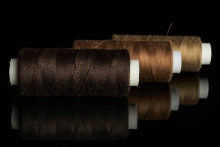 Group of three whole haberdashery item thread spools in row isolated on black glass