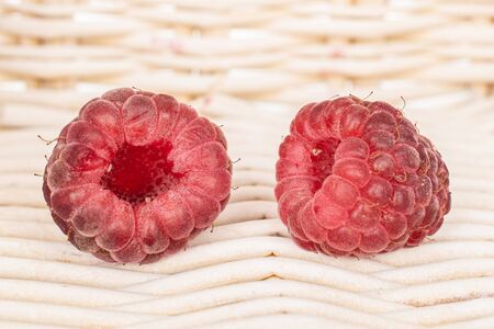 Group of two whole fresh crimson raspberry with braided rattan behind