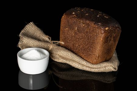 One whole fresh baked dark bread with jute bag and pinch of salt isolated on black glass