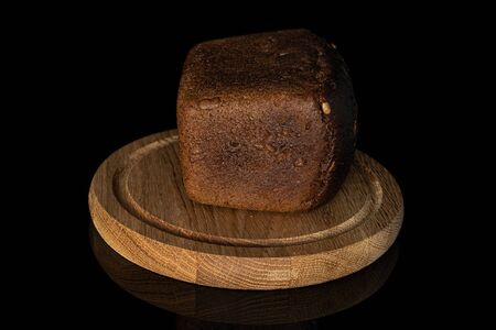 One whole fresh baked dark bread on bamboo plate isolated on black glass