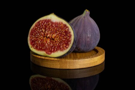 Group of one whole one half of fresh purple fig on bamboo coaster isolated on black glassの写真素材
