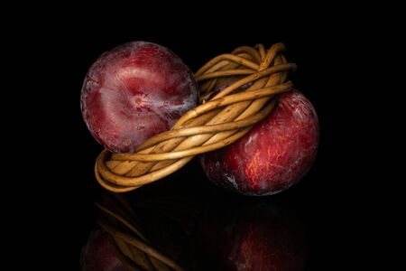 Group of two whole fresh red plum in wiker nest isolated on black glassの写真素材