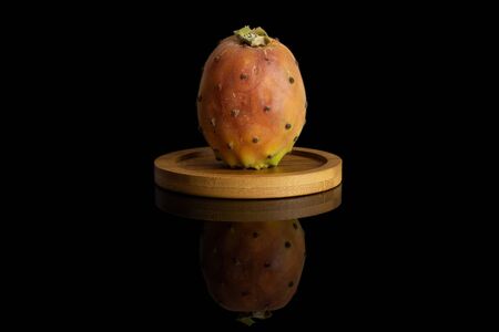 One whole fresh orange opuntia on bamboo coaster isolated on black glassの写真素材