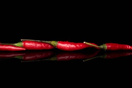 Group of four whole hot red chili isolated on black glass