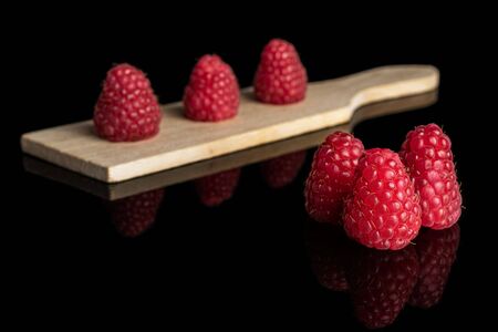 Group of six whole fresh red raspberry on small wooden cutting board isolated on black glassの写真素材