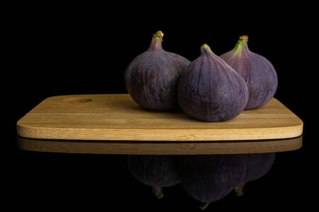 Group of three whole fresh purple fig on bamboo cutting board isolated on black glass